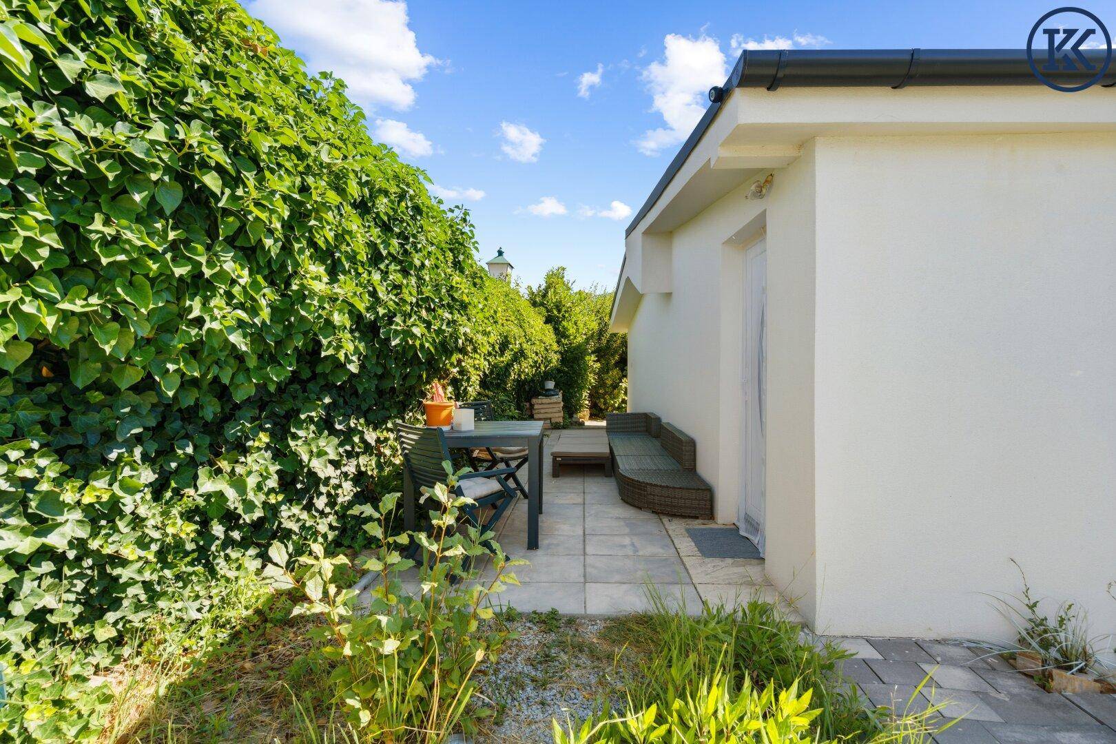 Gepflasterte Terrasse mit Gartenmöbeln und einer hohen grünen Hecke, die Privatsphäre bietet.