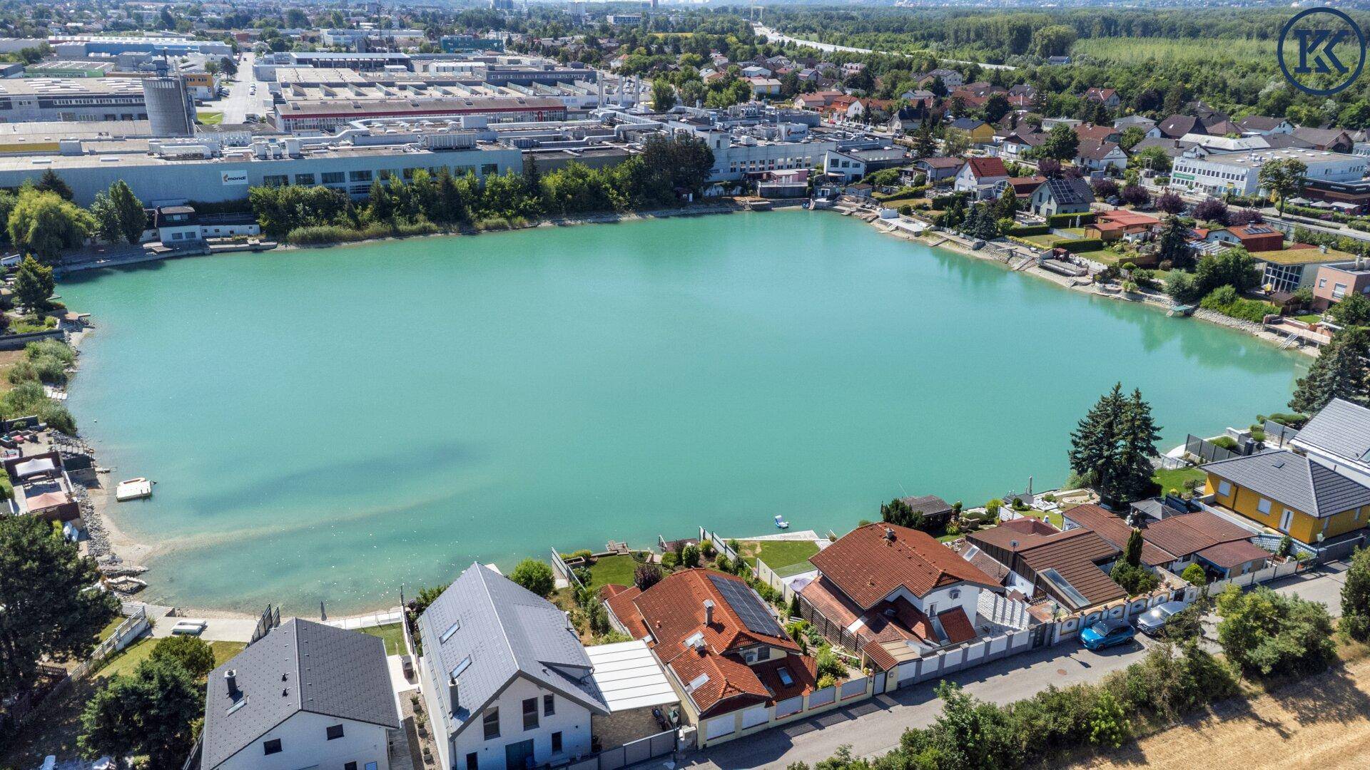 Weitläufige Luftaufnahme des Sees und der umliegenden Wohn- und Industriegebiete an einem sonnigen Tag.
