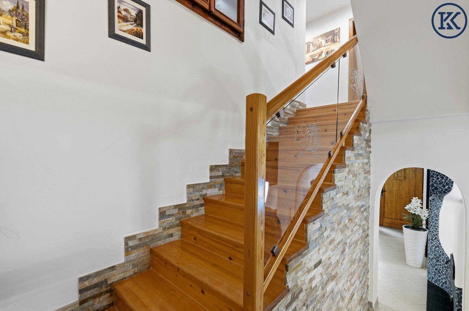Holztreppe mit Glasgeländer und Steinwandverkleidung, die die Stockwerke verbindet.