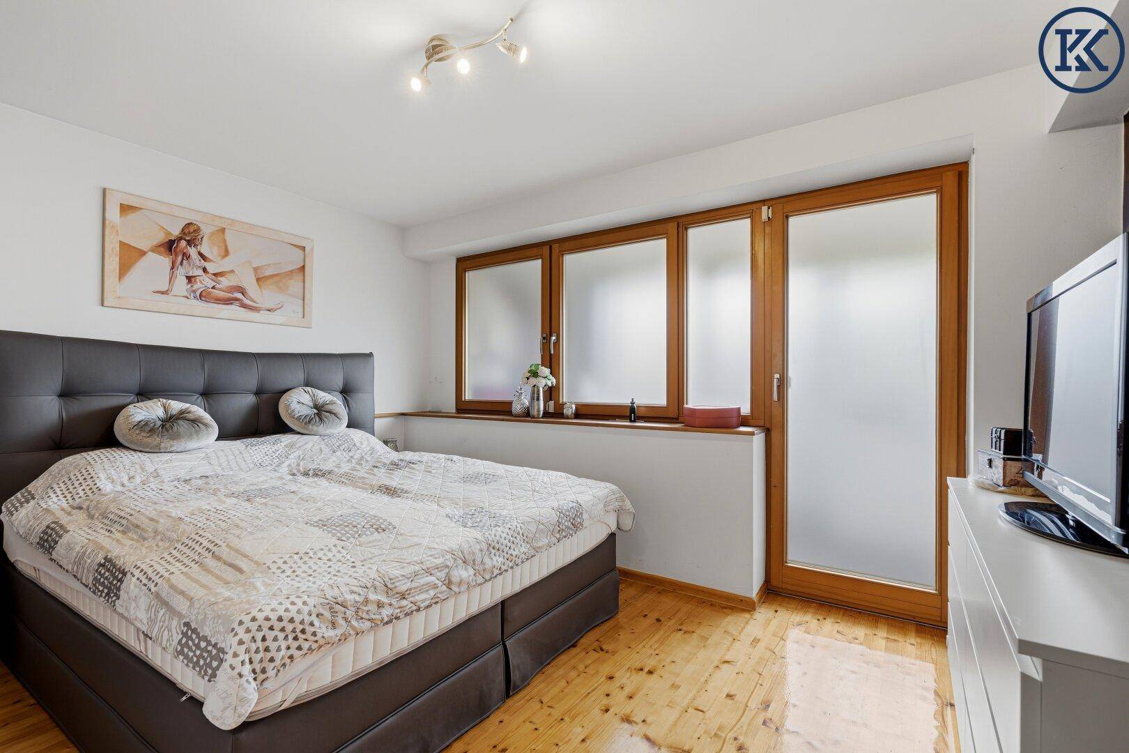 Gemütliches Schlafzimmer mit Doppelbett, Holzboden und großen Fenstern.