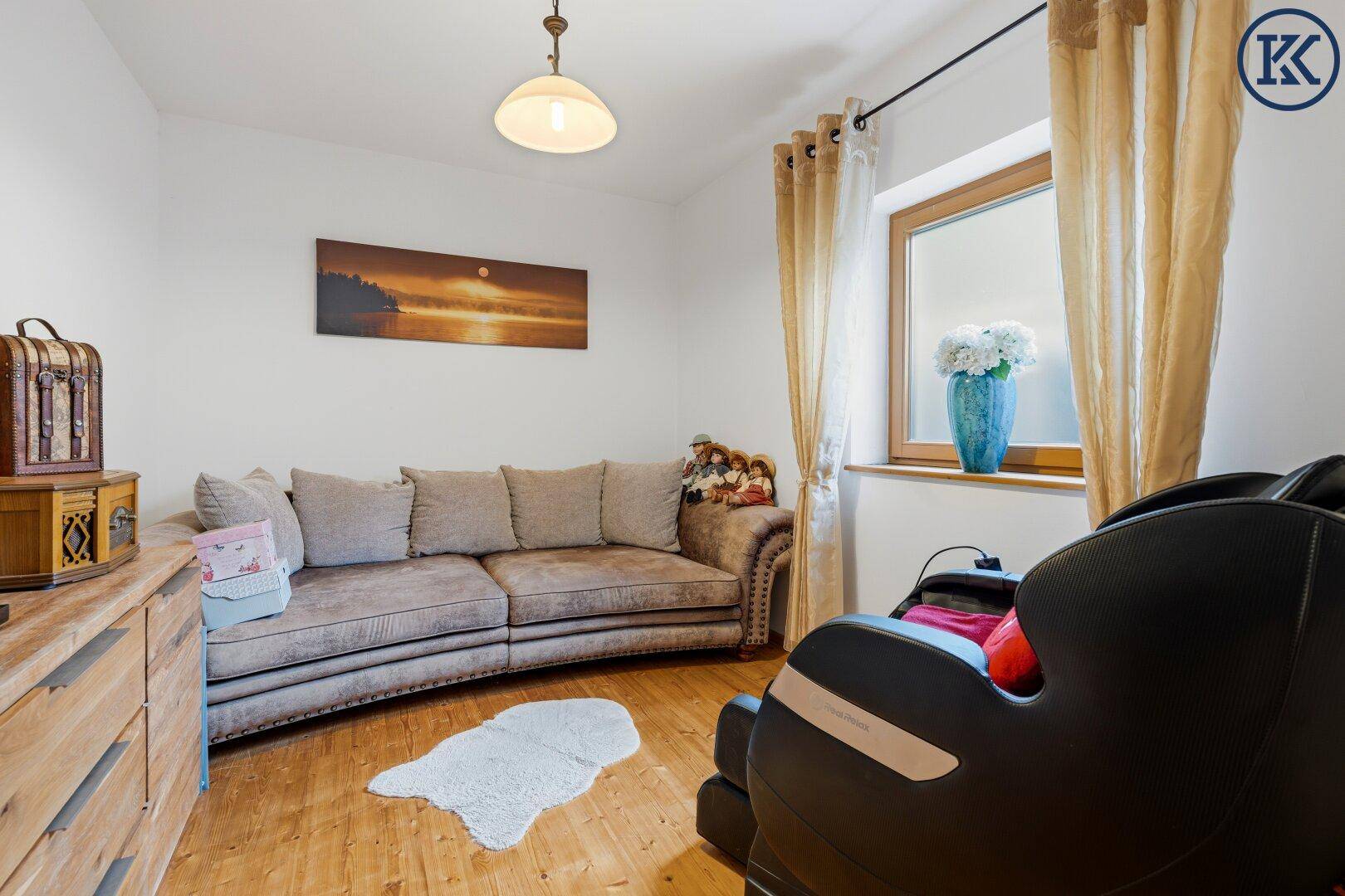 Gemütliches Wohnzimmer mit Holzboden, beigem Sofa und einem Fenster, das natürliches Licht hereinlässt.