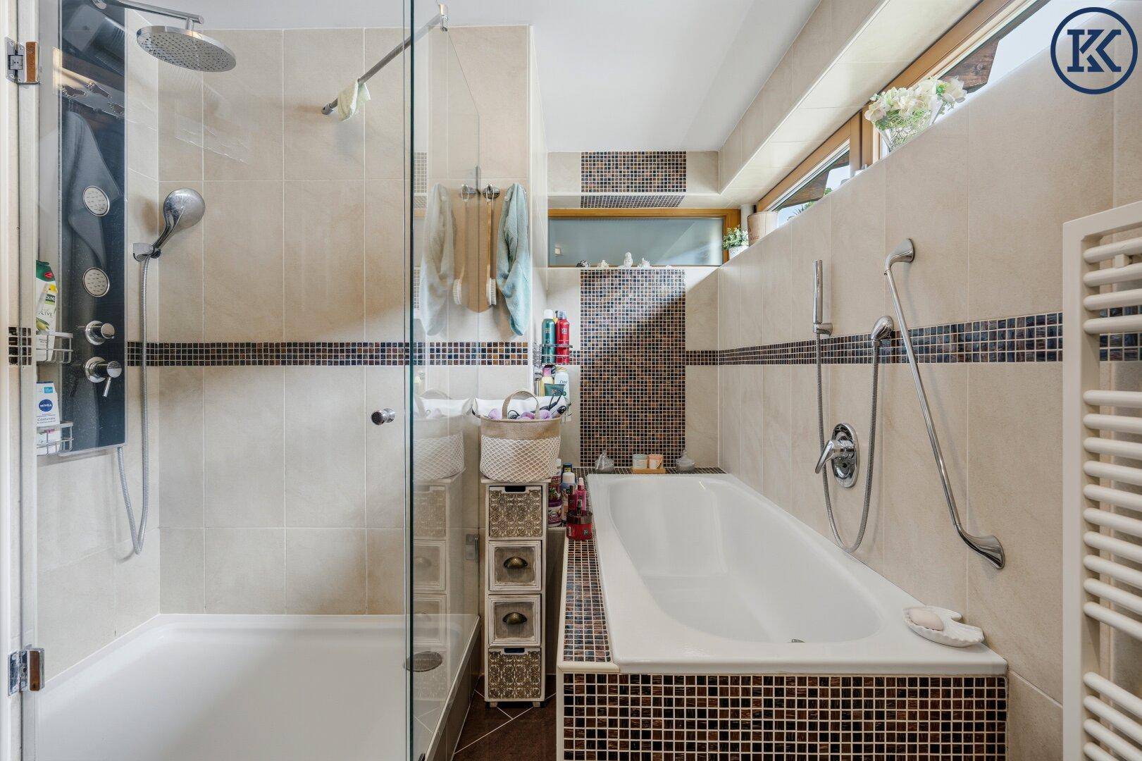 Geräumiges Badezimmer mit Badewanne, separater Duschkabine und beigen Fliesen mit dunklen Akzenten.