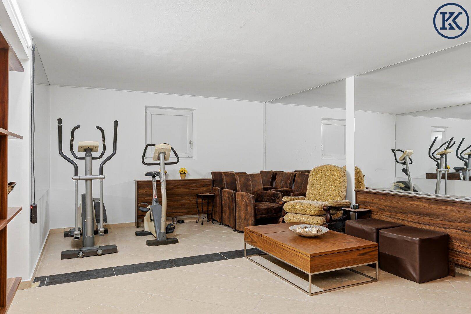 Fitnessraum im Keller mit Trainingsgeräten, Sitzgelegenheiten und einem großen Spiegel.
