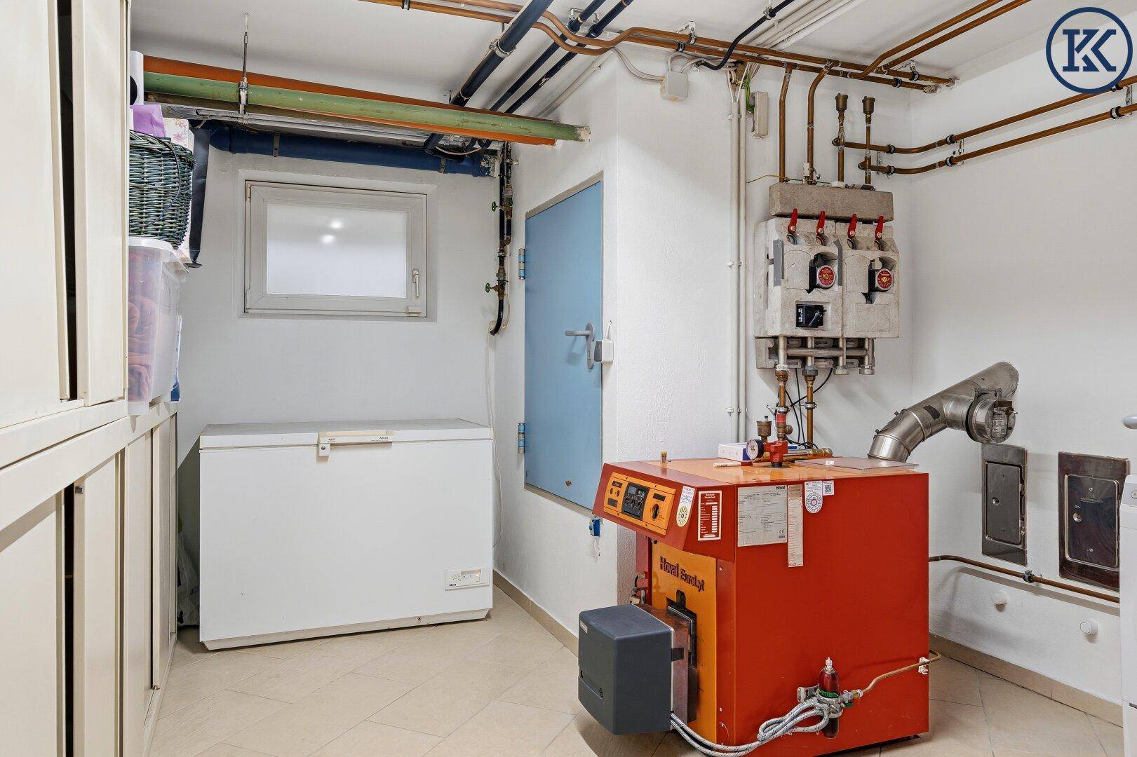 Heizungsraum im Keller mit Heizkessel, Rohren und einem Gefrierschrank für Lagerung.