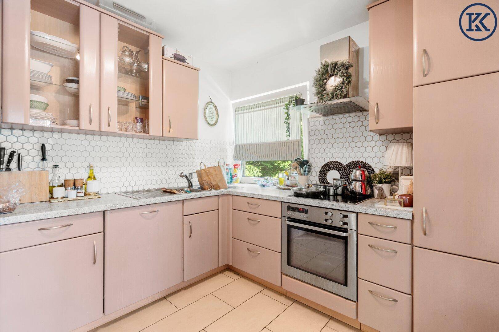 Charmante rosa Küche mit Backofen, Dunstabzugshaube und viel Tageslicht.