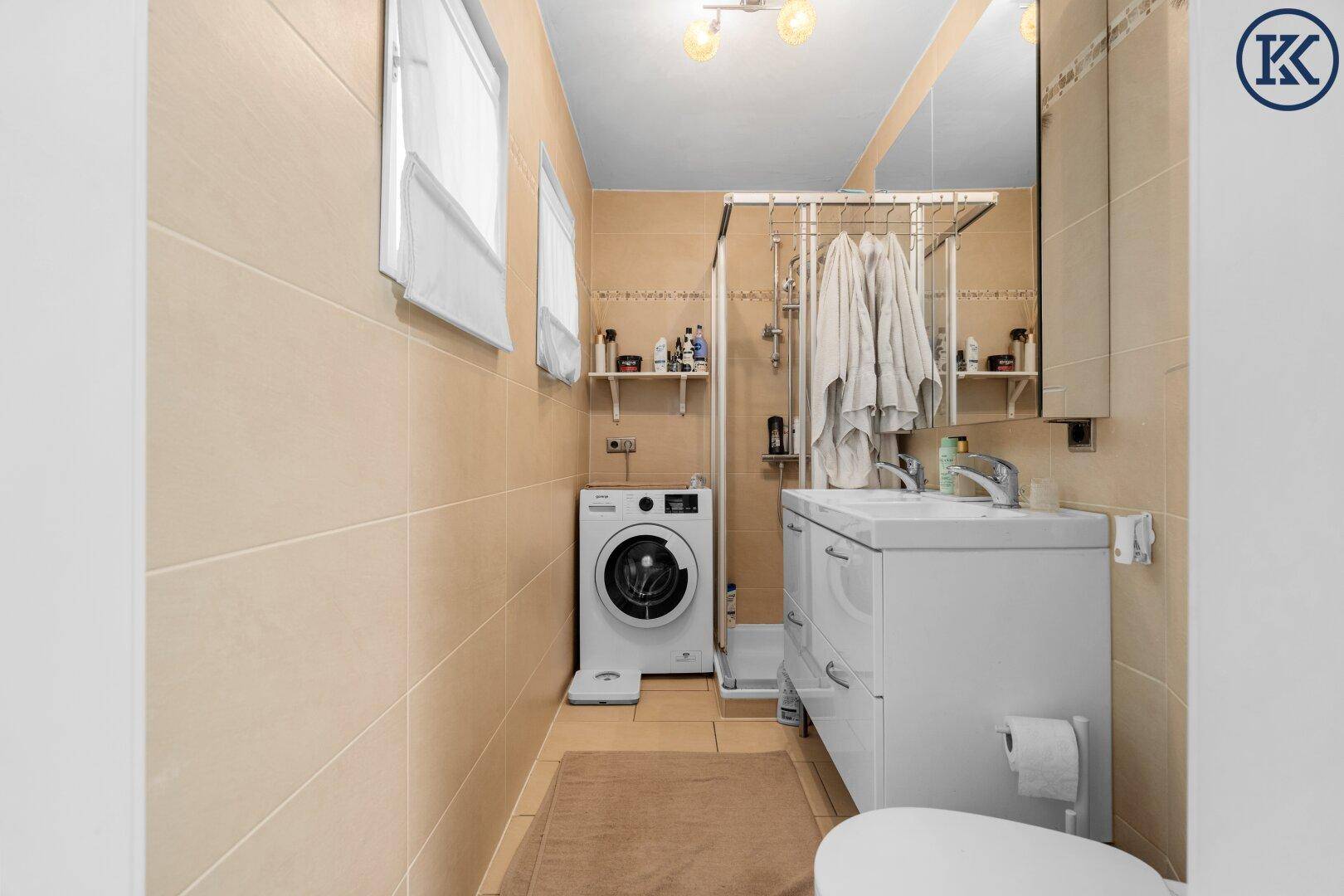 Modernes Badezimmer mit Dusche, Waschmaschine und beigefarbenen Fliesen.