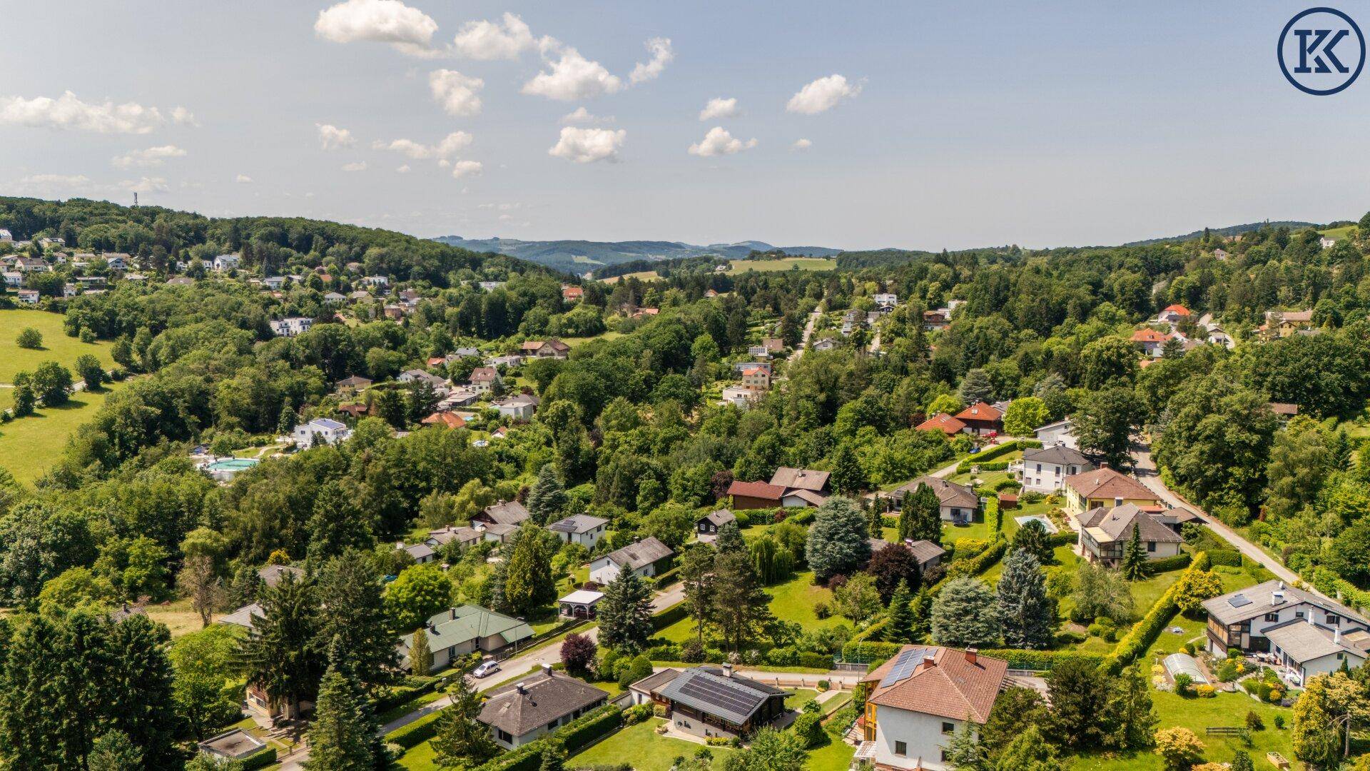 Weitläufige Wohngegend mit vielen Häusern und üppiger grüner Landschaft unter blauem Himmel.