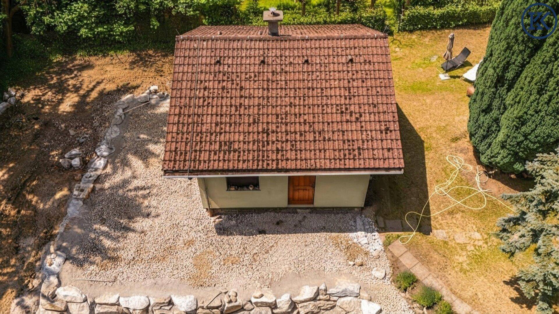 Kleines Haus mit Ziegeldach und Kiesfläche, umgeben von Bäumen und Natur.