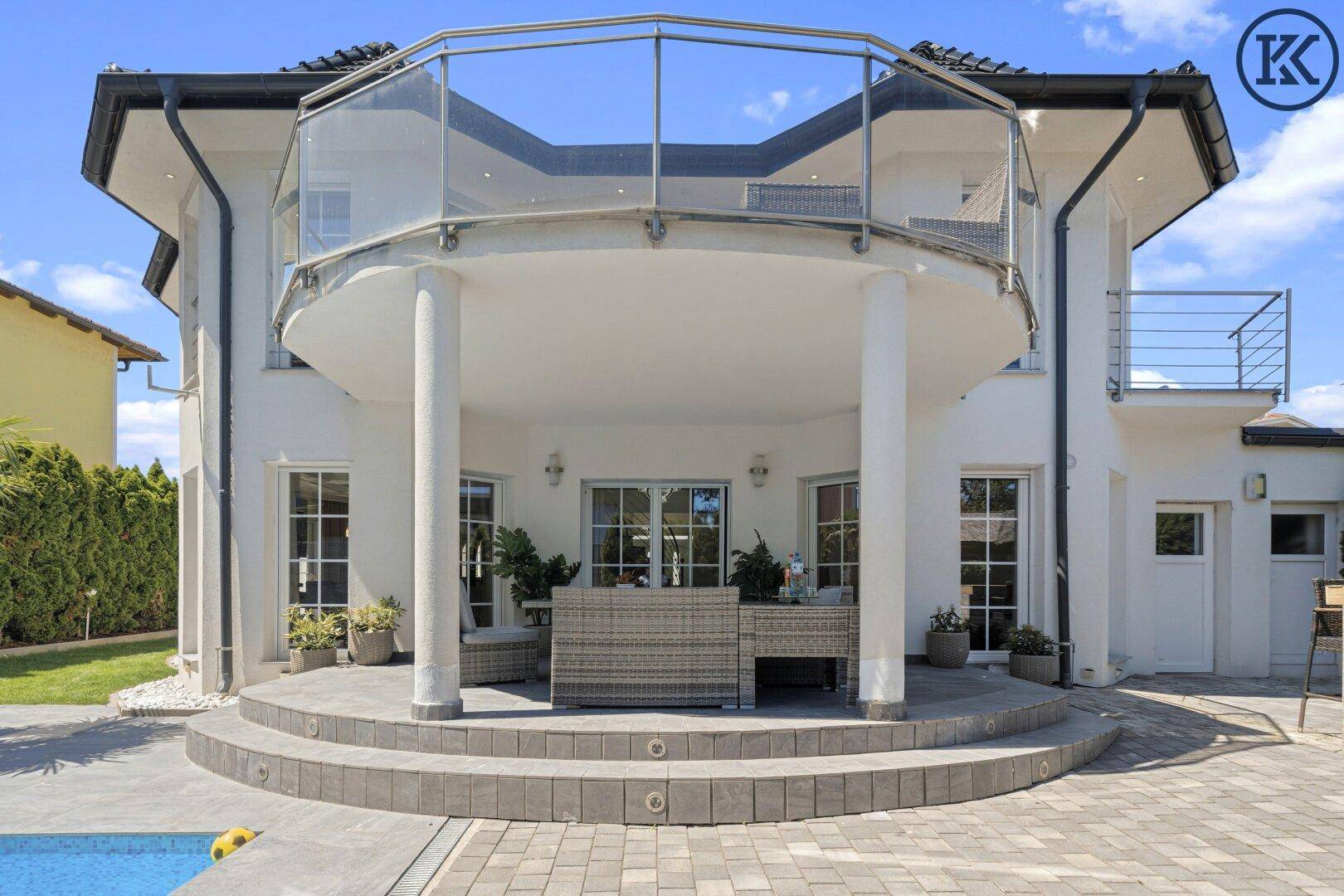 Rückseite des Hauses mit großem Balkon, Glasgeländer und einer eleganten Treppe zum Garten.
