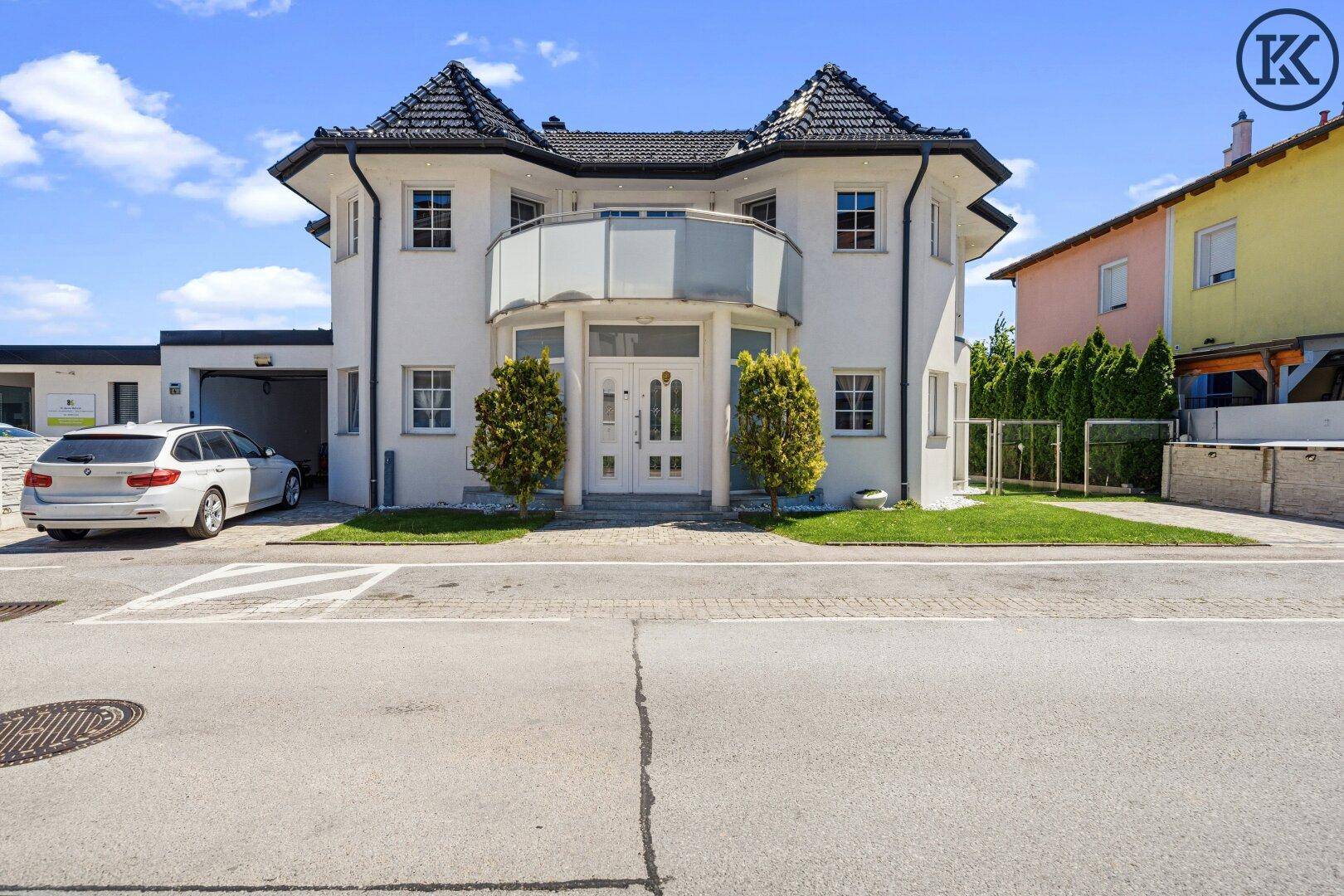 Elegantes Einfamilienhaus mit markantem Dach, geschwungenem Balkon und gepflegtem Vorgarten.