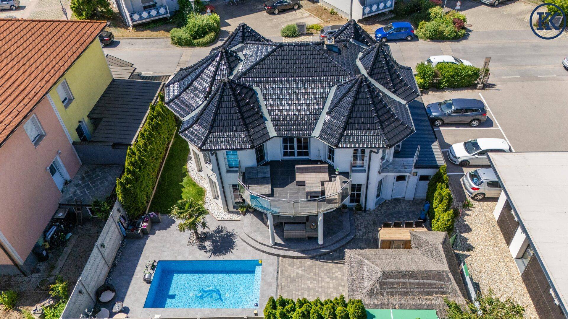 Luftaufnahme des Anwesens mit markantem Dach, Poolbereich und umliegender Nachbarschaft.