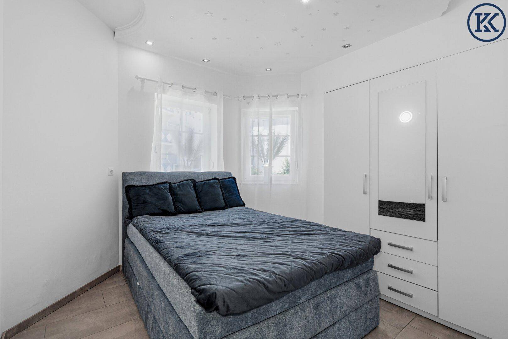 Schlafzimmer mit blauem Boxspringbett, weißem Kleiderschrank und hellen Fliesen.