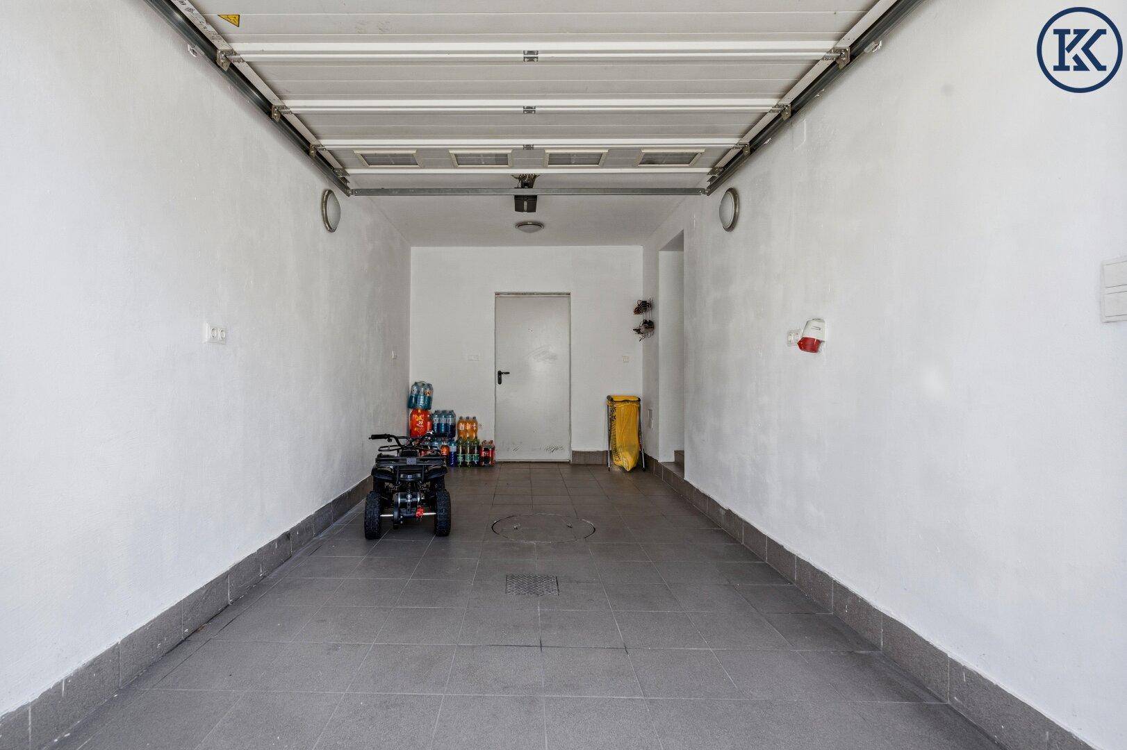 Geräumige Garage mit Fliesenboden und automatischem Garagentor, bietet viel Stauraum.