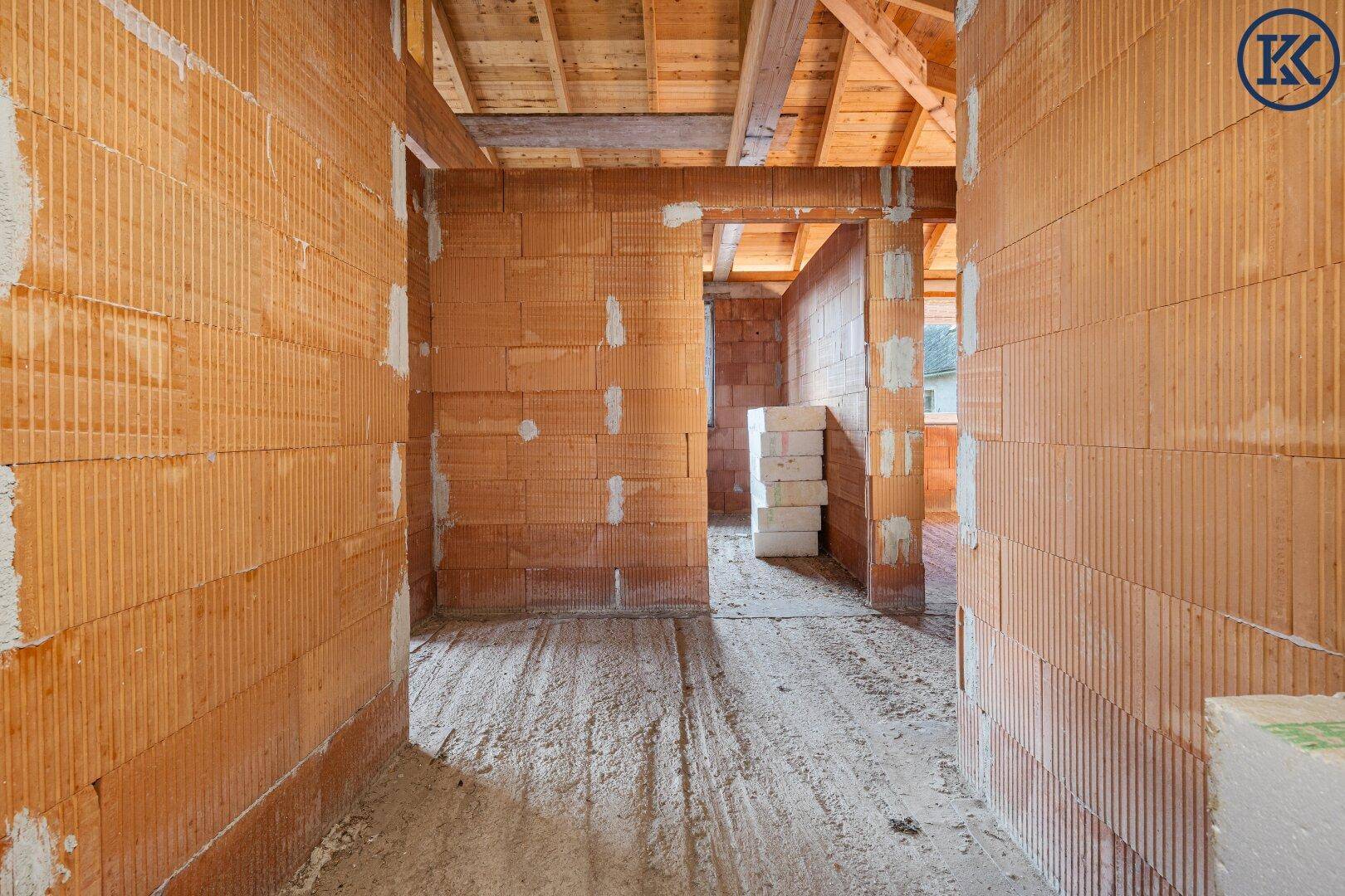 Innenansicht eines Raumes im Rohbau mit Blick auf weitere Zimmer und die Holzdecke.