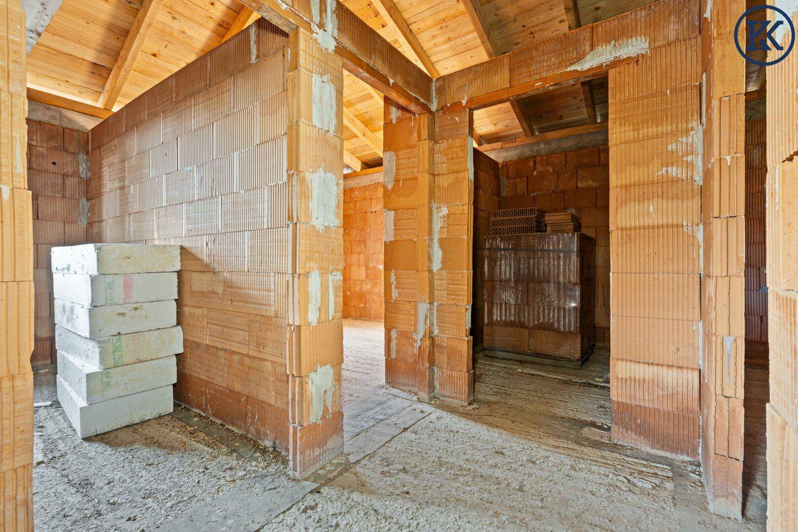 Rohbau eines Zimmers mit gestapelten Baumaterialien und sichtbaren Ziegelwänden.