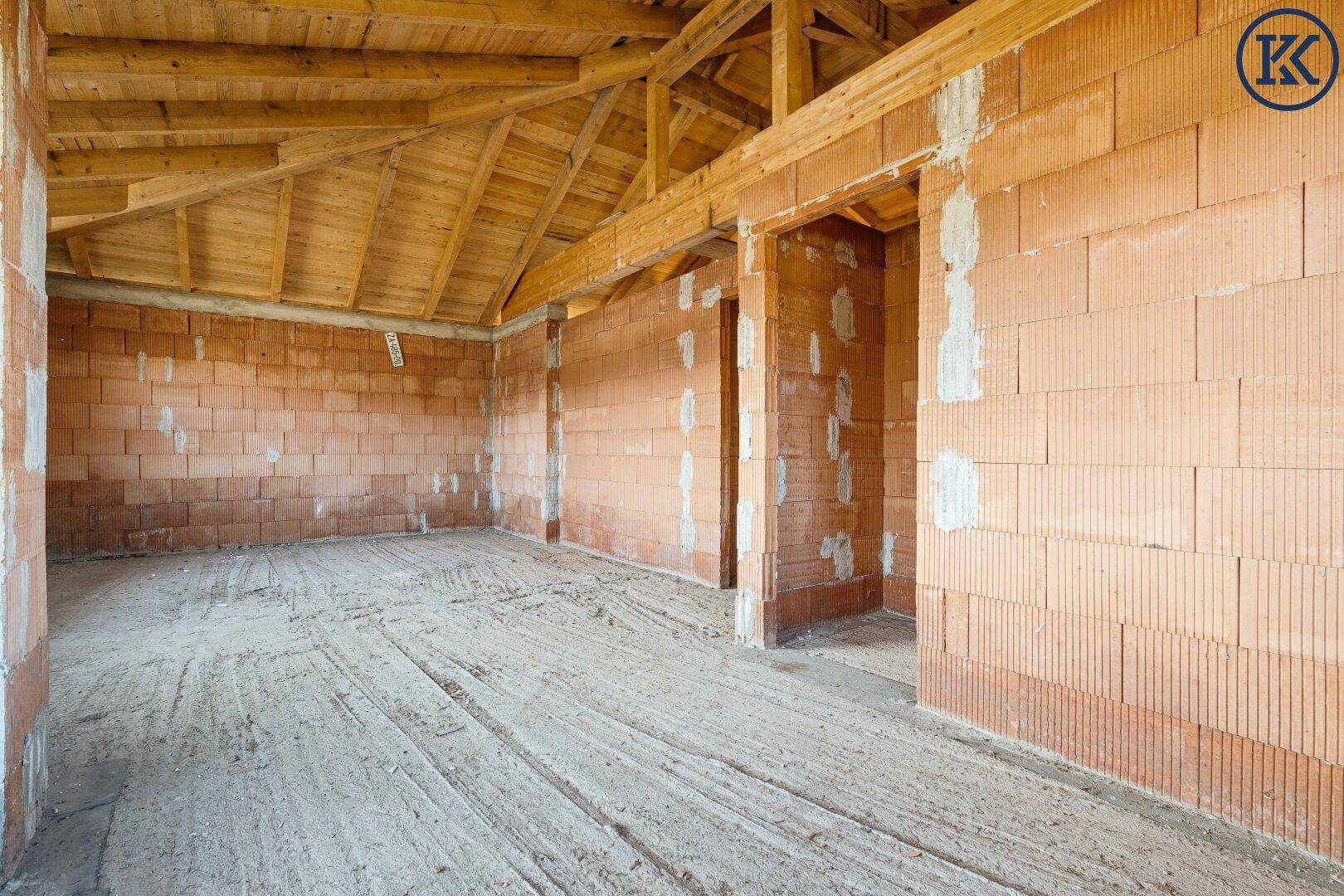 Innenansicht eines Rohbaus mit Ziegelwänden und einer offenen Holzdeckenkonstruktion.
