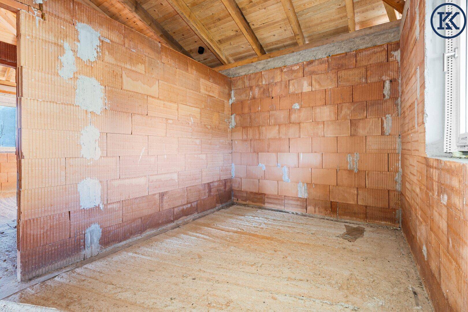Rohbau eines Raumes mit Ziegelwänden und sichtbarer Holzdeckenkonstruktion, bereit für den Ausbau.