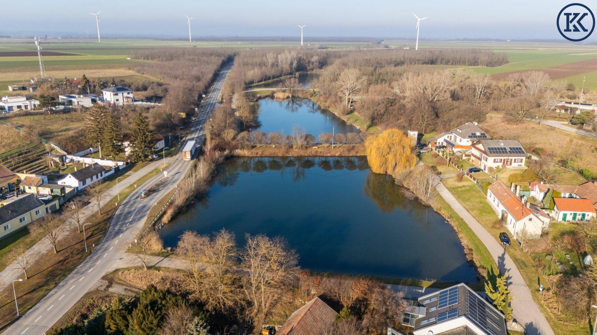 Luftaufnahme einer ländlichen Gegend mit Seen, Häusern und Windkraftanlagen in der Ferne.