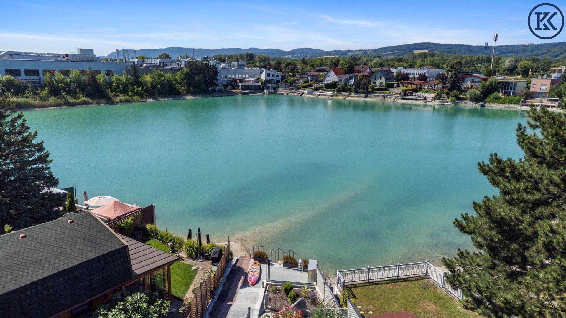 Nahaufnahme des Seeufers mit privaten Zugängen und angrenzenden Wohnhäusern unter blauem Himmel.