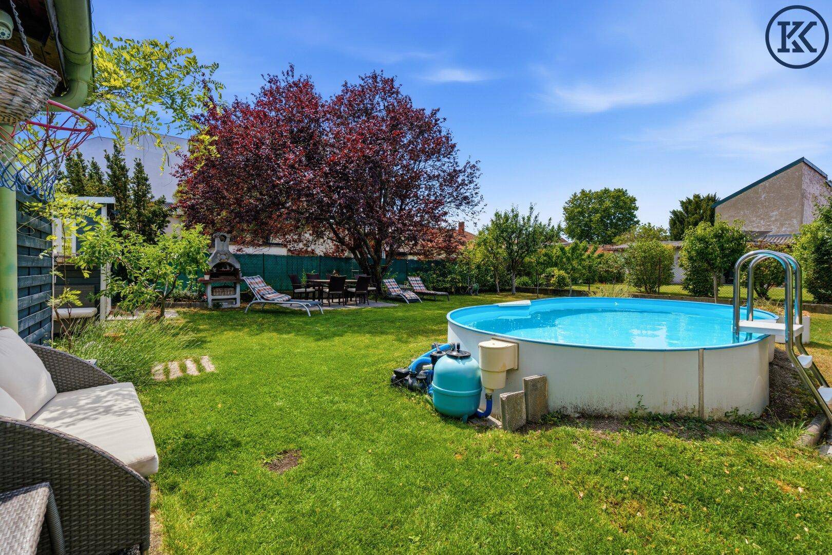 Großer Garten mit Pool, Grillplatz und Sitzgelegenheiten unter einem schattenspendenden Baum.
