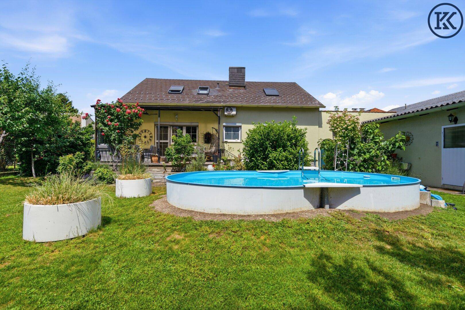 Hinterhof mit großem Aufstellpool und weitläufiger Rasenfläche unter blauem Himmel.