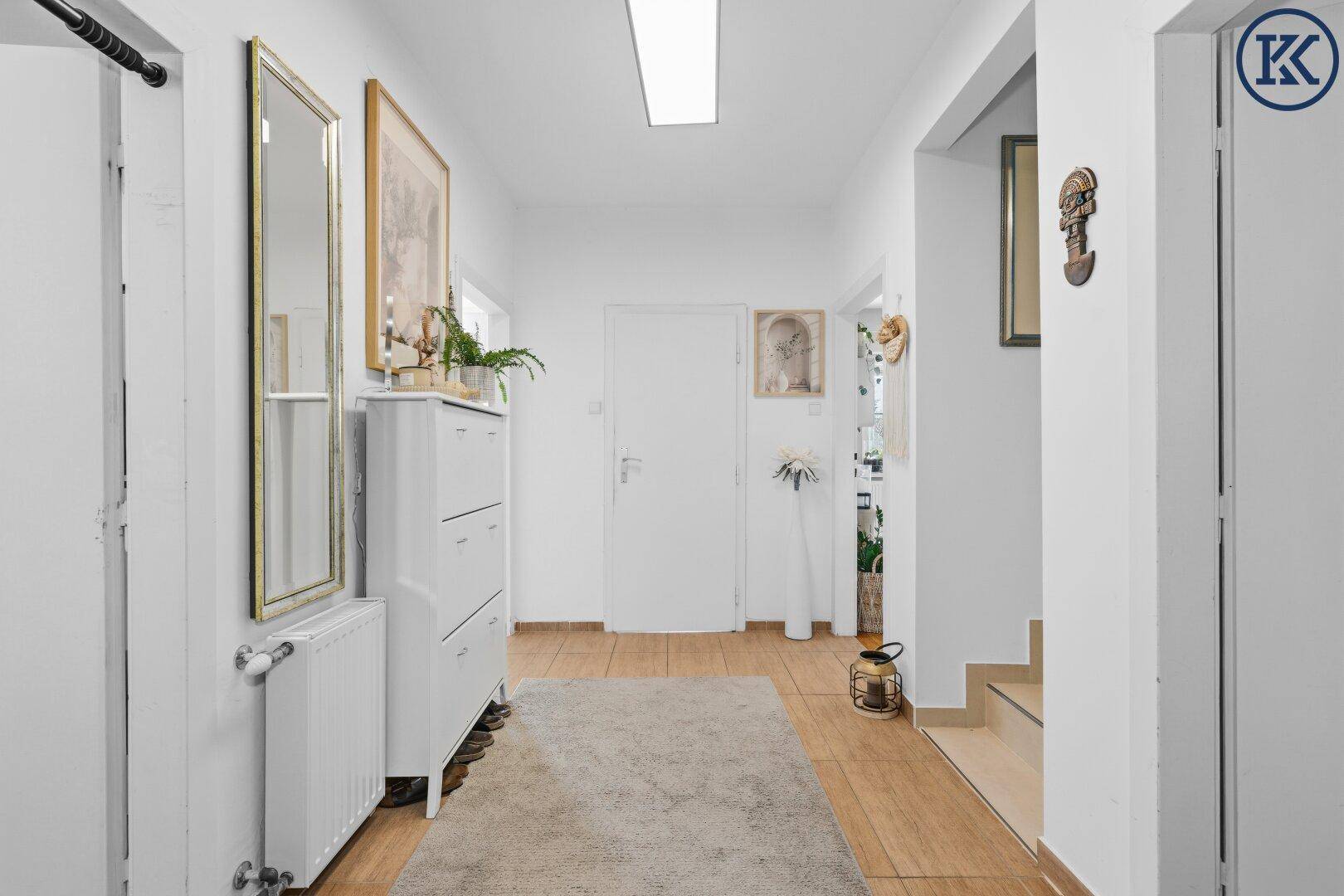 Geräumiger Flur mit Holzfußboden, Teppich, Schuhschrank und großem Spiegel.