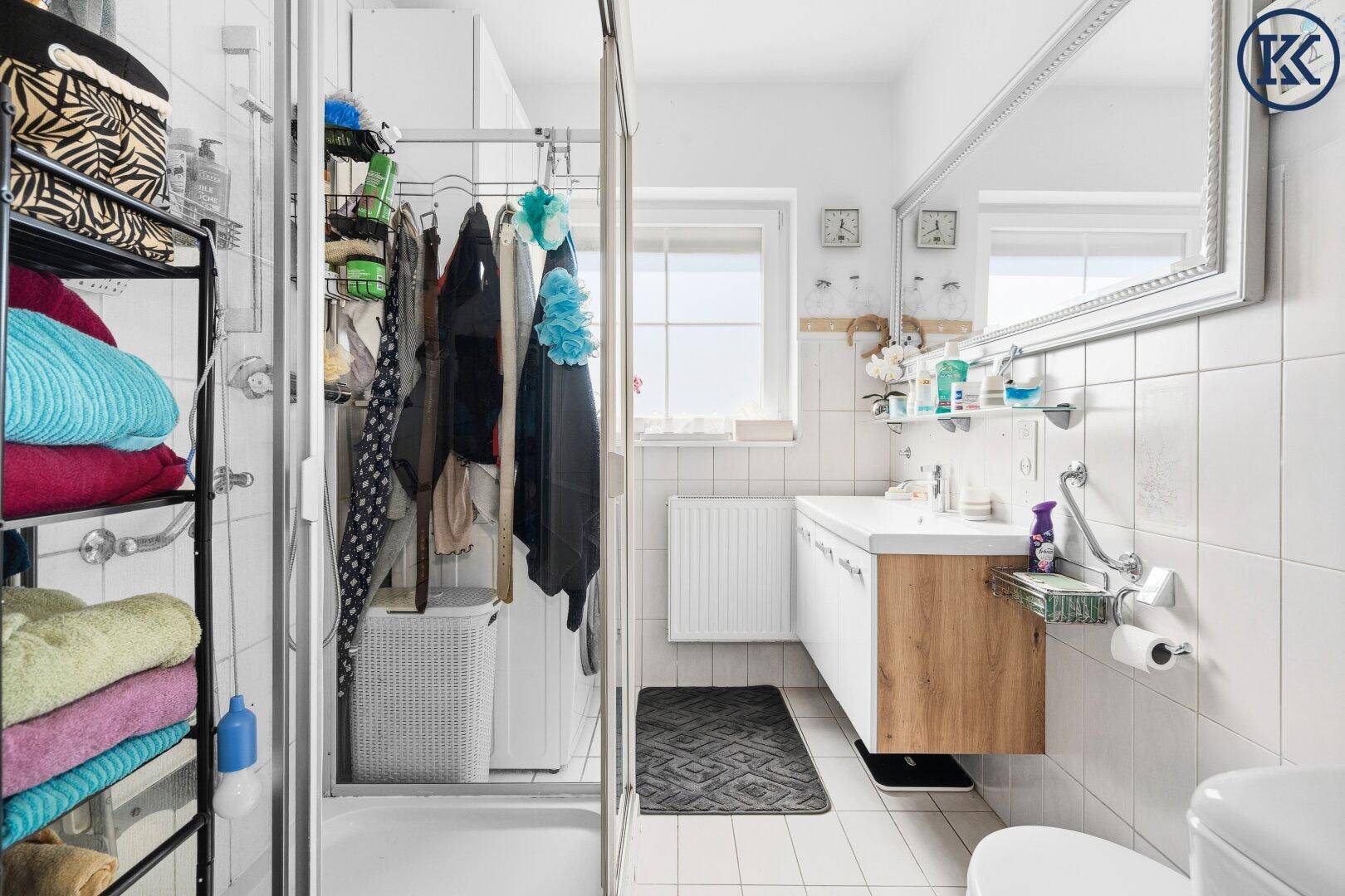 Helles Badezimmer mit Dusche, Waschbecken, Toilette und Fenster.