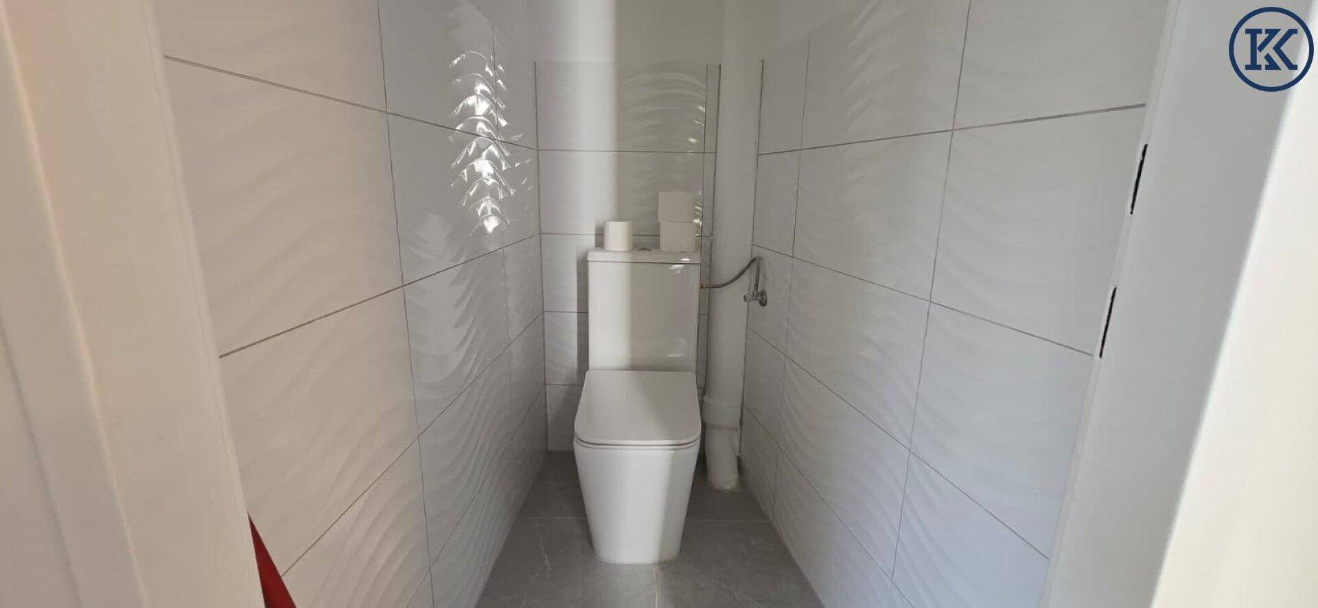 Kleines, hell gefliestes Gäste-WC mit wandmontierter Toilette und schlichtem Design.