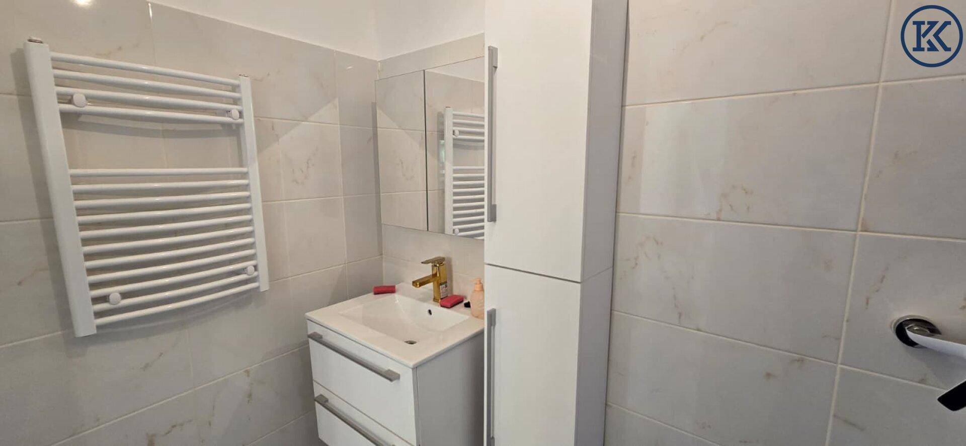 Helles Badezimmer mit weißem Handtuchheizkörper, Einzelwaschbecken und Spiegelschrank.
