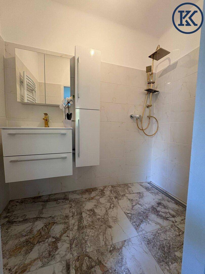 Modernes Badezimmer mit begehbarer Dusche, eleganten Goldarmaturen und stilvollem Fliesenboden.