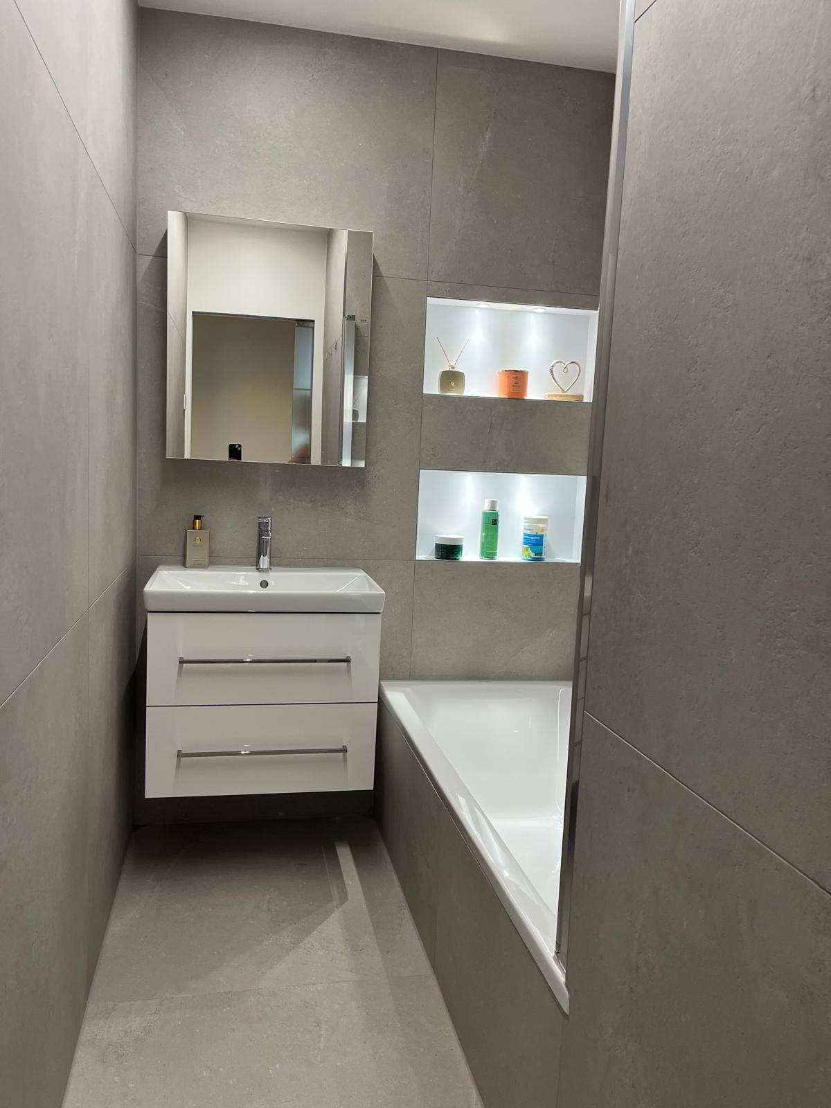 Helles Badezimmer mit grauen Fliesen, Waschtisch mit Spiegel und Badewanne.
