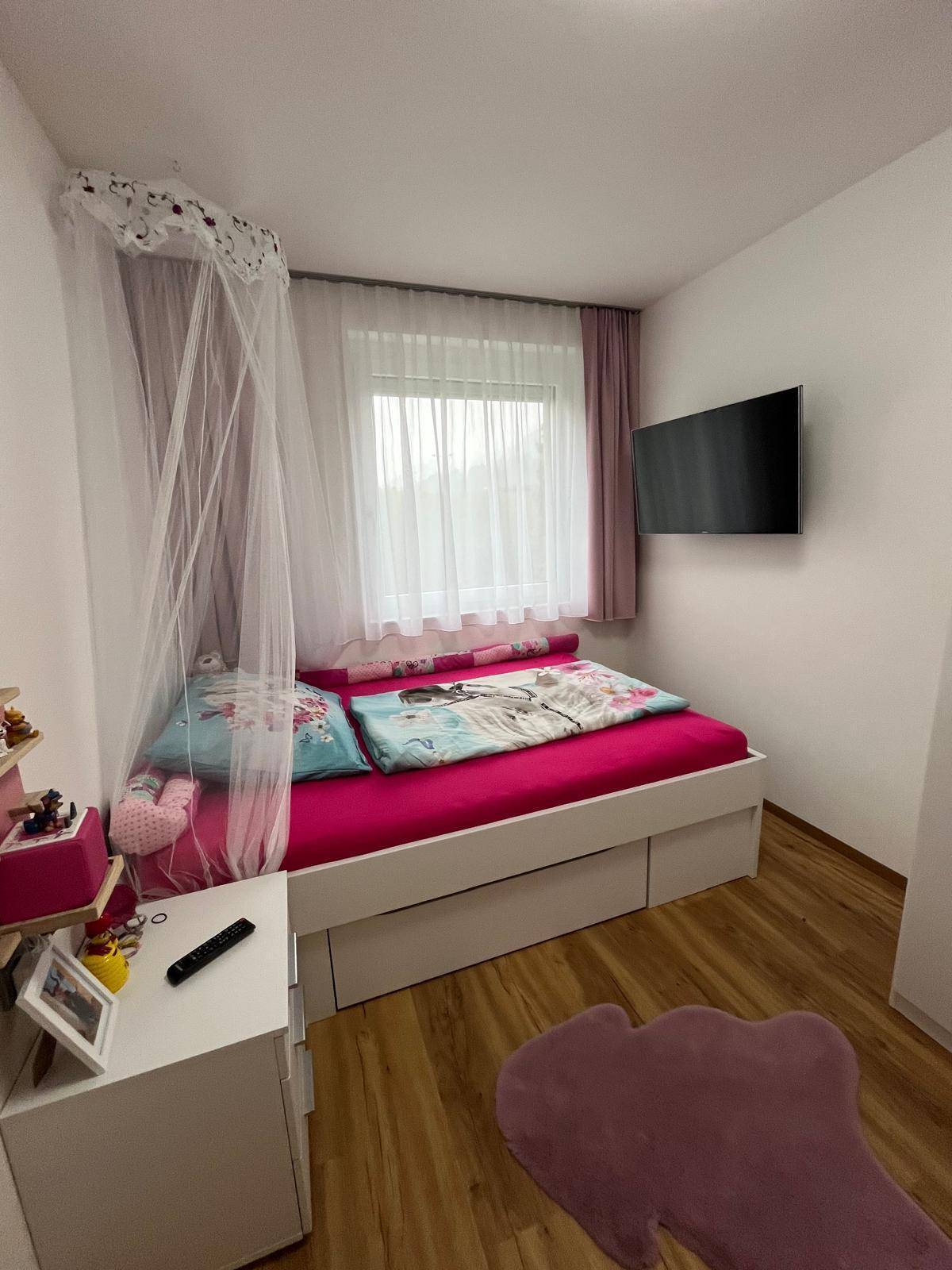 Kinderzimmer mit Einzelbett, Himmelbett, rosa Bettwäsche und wandmontiertem Fernseher.