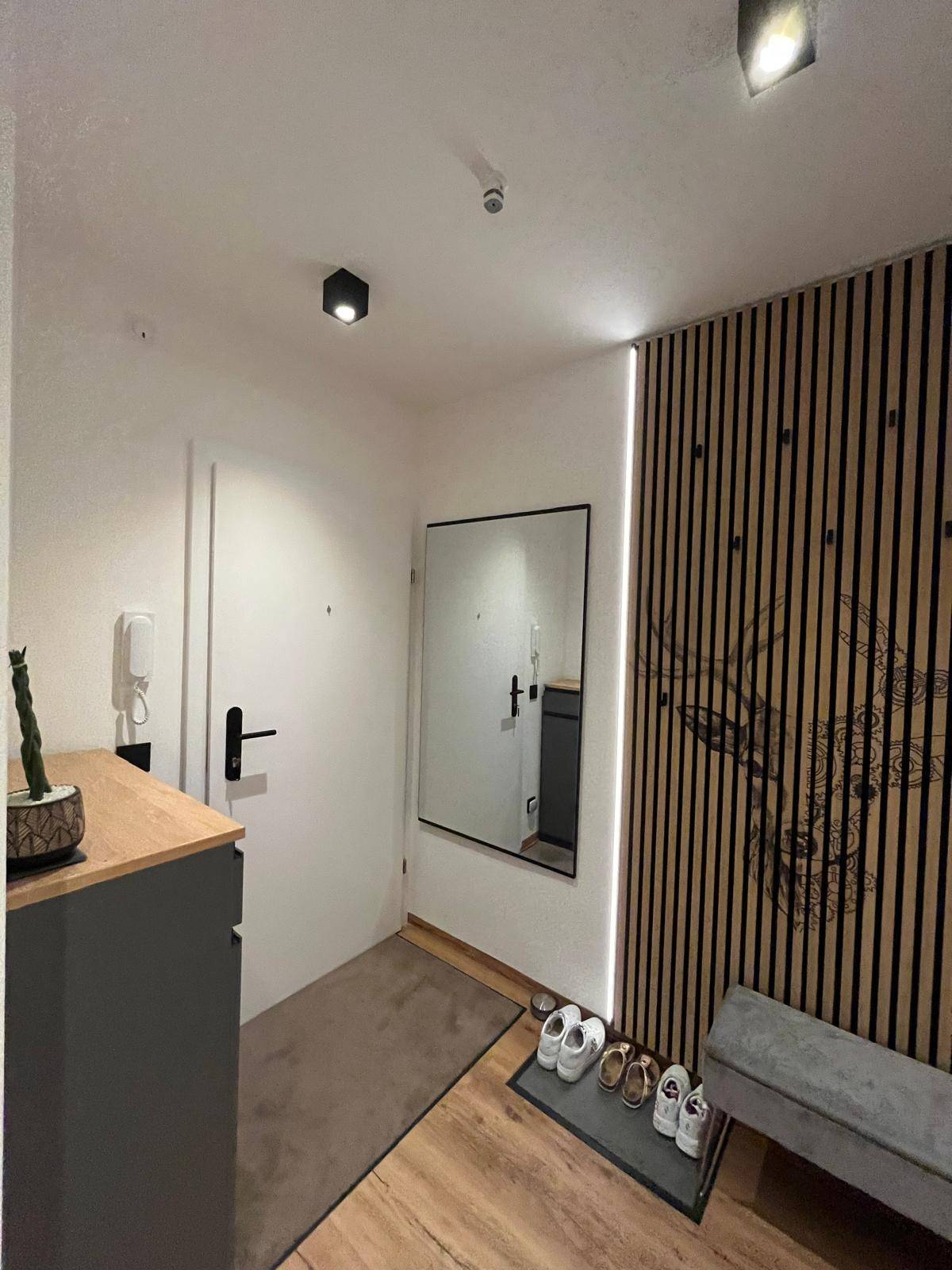 Eingangsbereich mit Holzlamellenwand, großem Spiegel und moderner Kommode für zusätzlichen Stauraum.