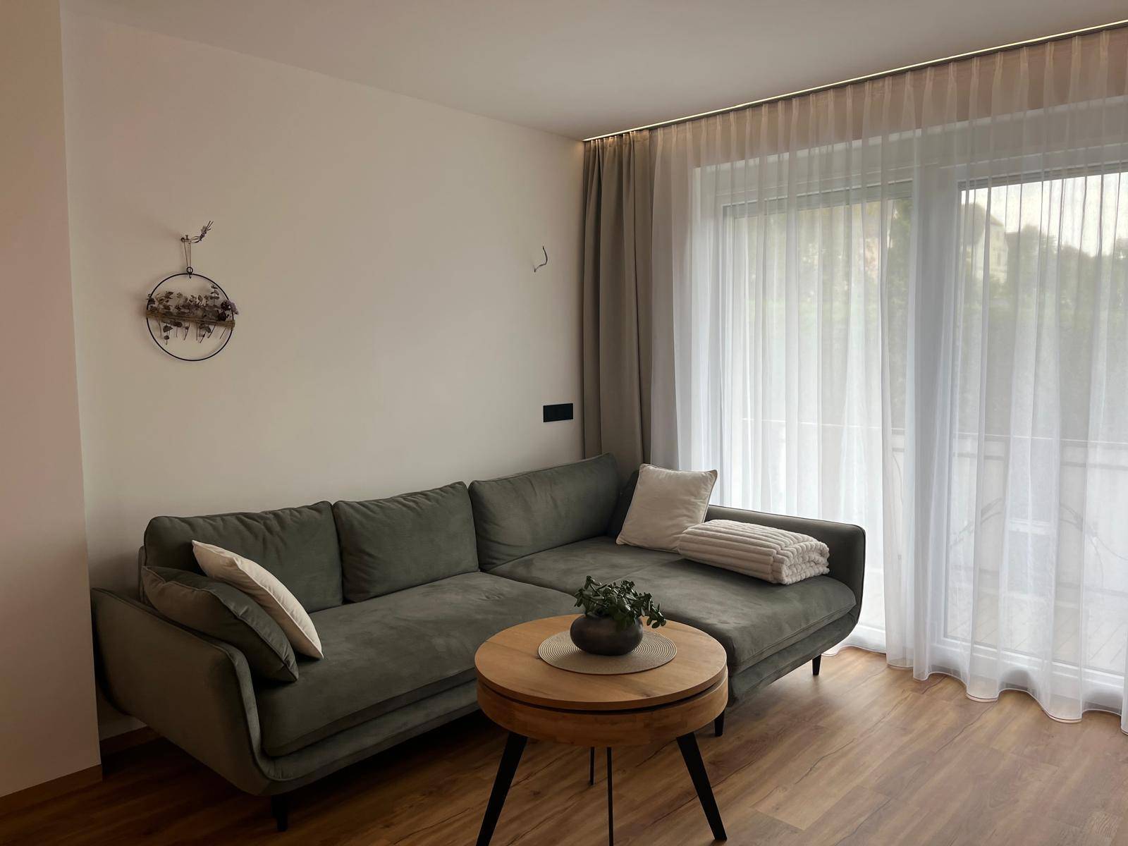 Gemütliches Ecksofa in einem hellen Wohnzimmer mit Holzboden und Vorhängen.