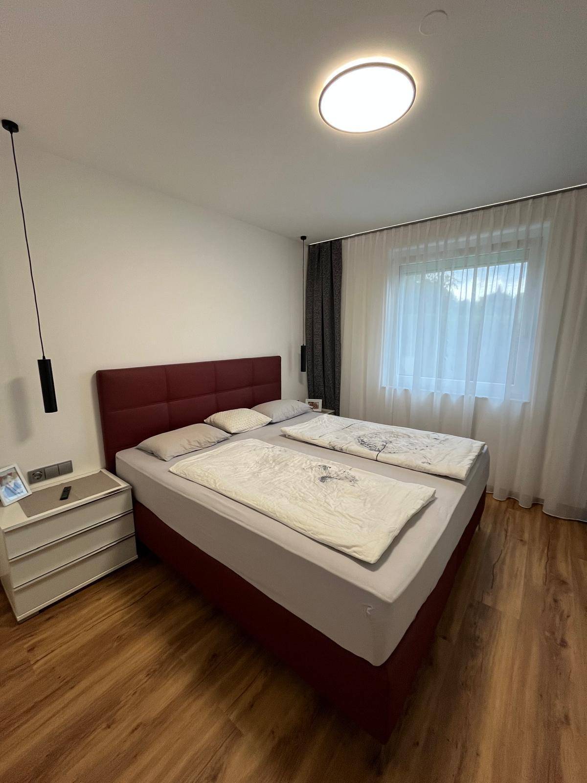 Helles Schlafzimmer mit Doppelbett, Nachttisch und großem Fenster für viel Tageslicht.
