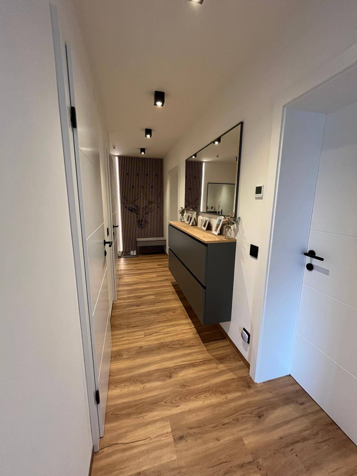 Stilvoller Flur mit Laminatboden, schwebender Kommode und einer dekorativen Holzlamellenwand mit Hirschmotiv.