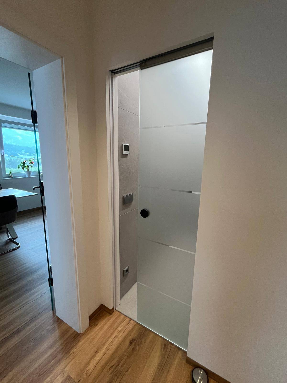 Moderner Flur mit Holzboden und einer satinierten Glasschiebetür zum Badezimmer.