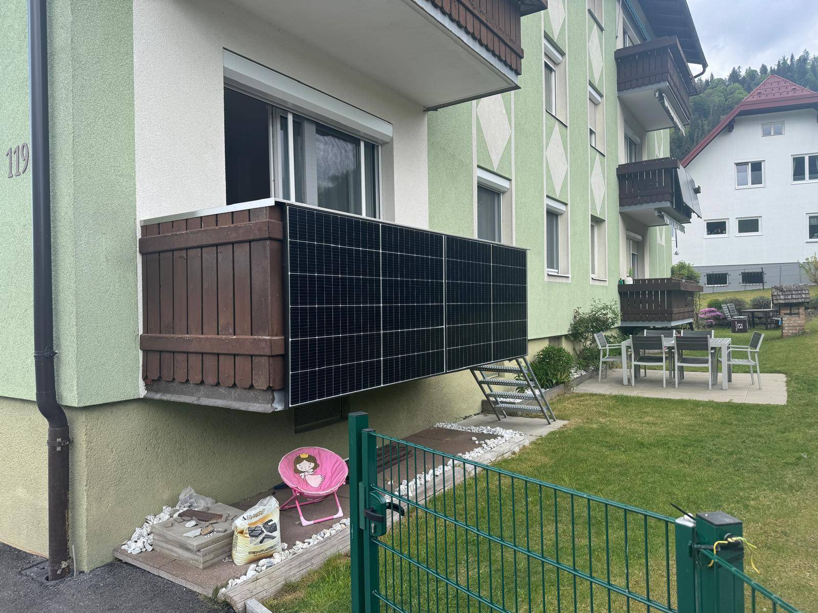 Balkon mit Solarmodulen an der Fassade eines Mehrfamilienhauses mit Garten.