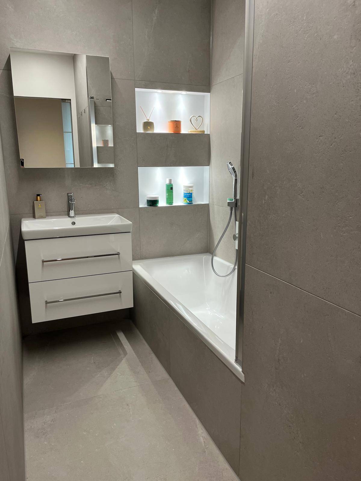 Modernes Badezimmer mit Badewanne, Duscharmatur und beleuchteten Nischen in der Wand.
