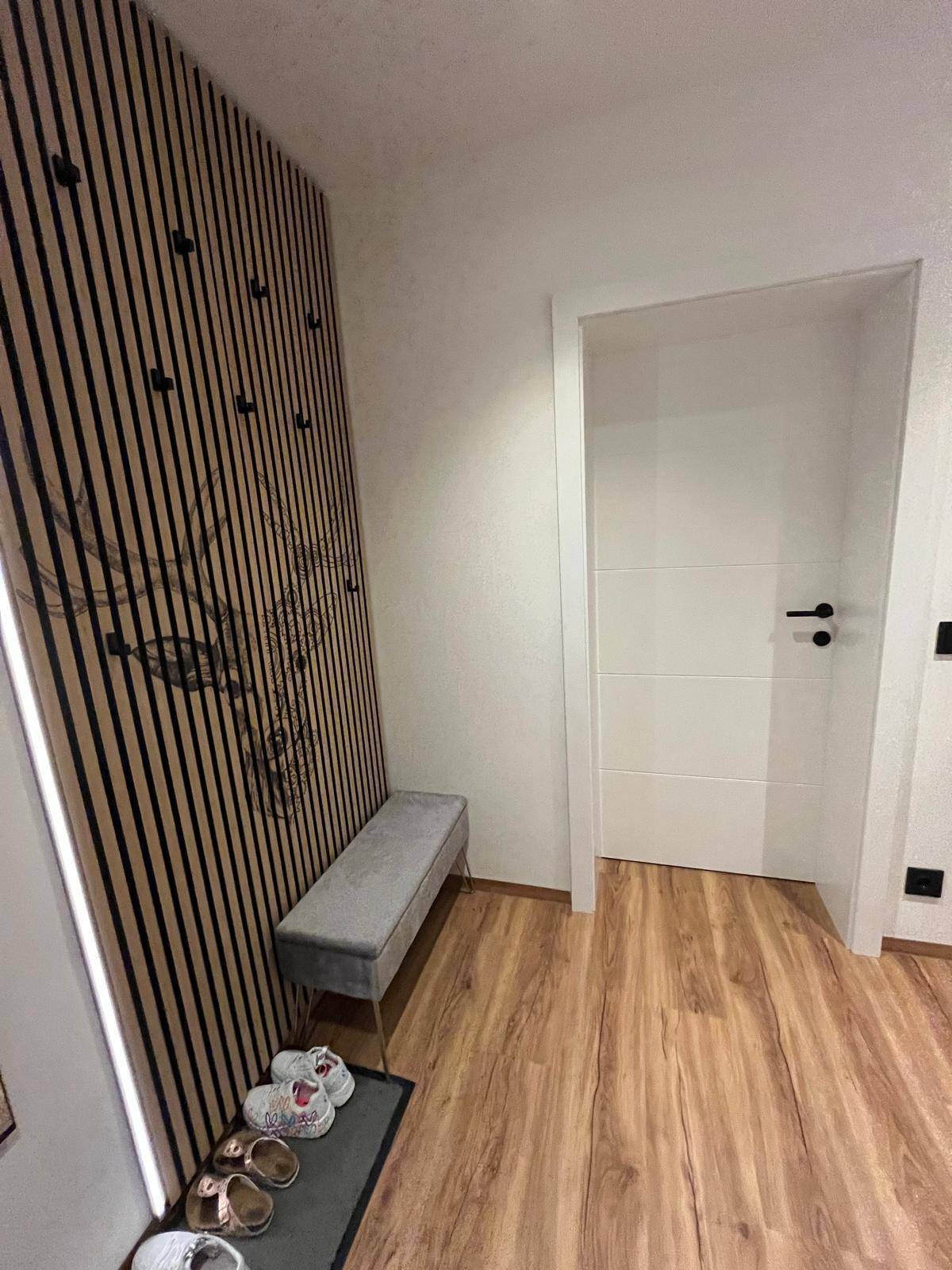 Eingangsbereich mit dekorativer Holzlamellenwand, Sitzbank und Laminatboden, ideal für Schuhe.