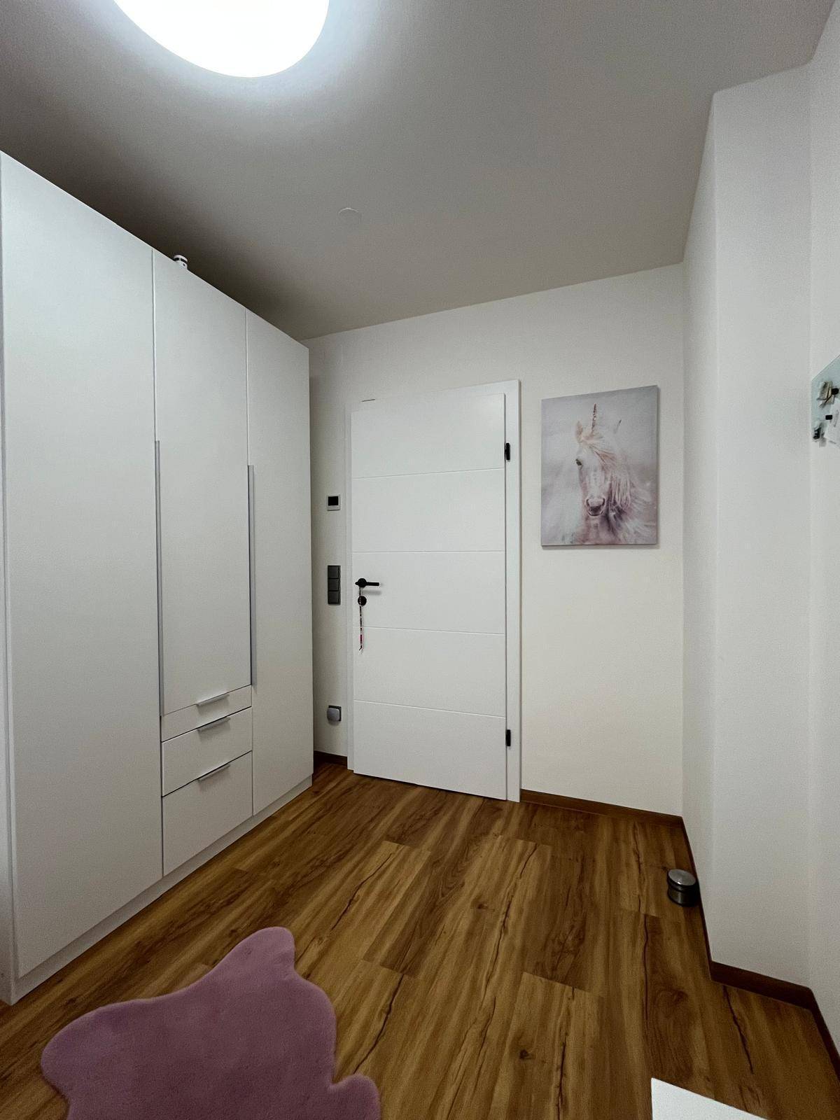 Heller Flur mit modernen weißen Einbauschränken und Laminatboden.