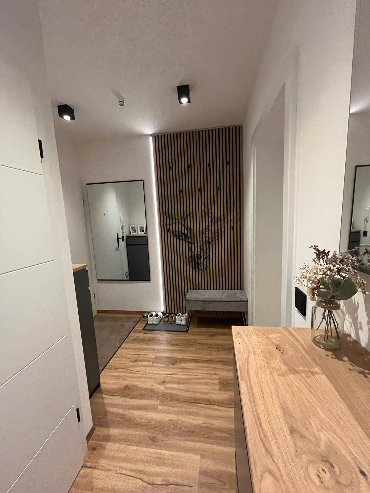 Eingangsbereich mit dekorativer Holzlamellenwand, Sitzbank, Spiegel und Laminatboden.