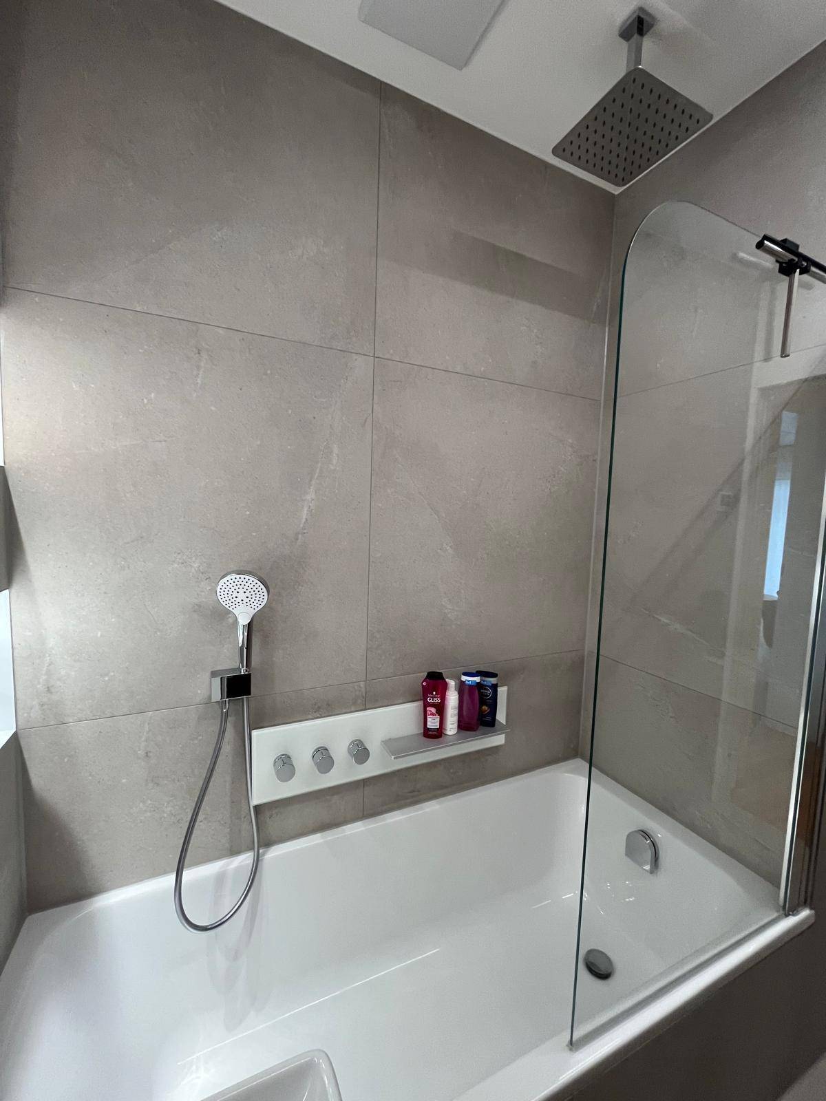 Modernes Badezimmer mit Badewanne, Duschabtrennung und Regendusche, gefliest in Grau.