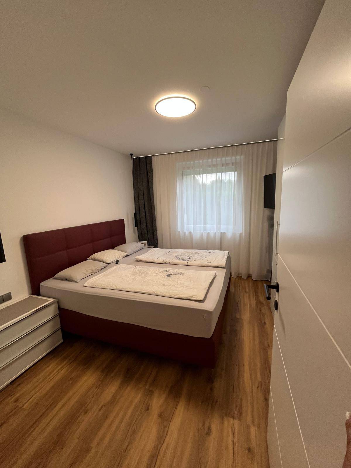 Schlafzimmer mit Doppelbett, Nachttisch und Fenster, das viel natürliches Licht hereinlässt.
