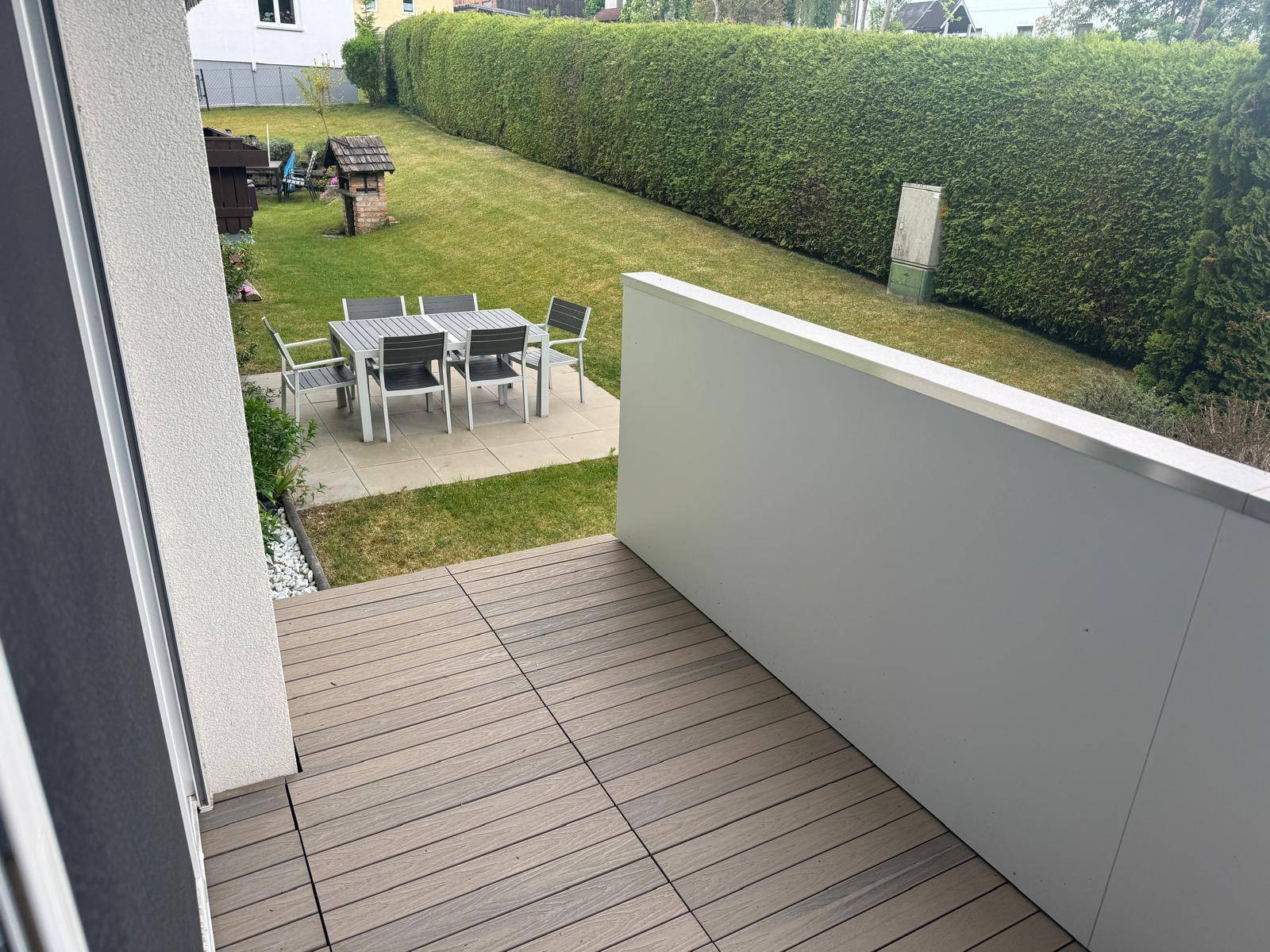 Große Terrasse mit Holzboden und Blick auf den Garten mit Sitzbereich und Hecke.