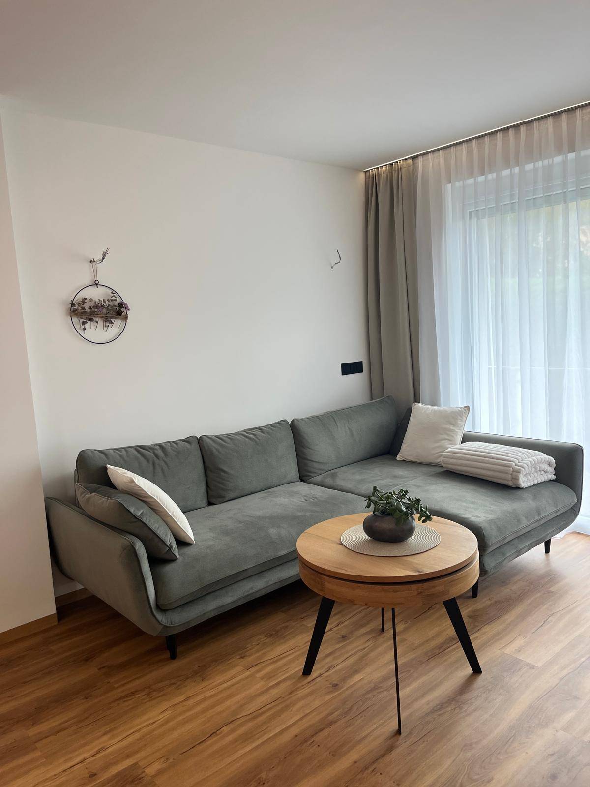 Gemütliches Ecksofa in einem hellen Wohnzimmer mit Holzboden und Vorhängen.