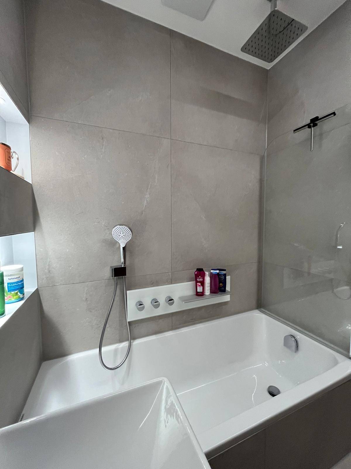 Modernes Badezimmer mit Badewanne, Regendusche und Handbrause, gefliest in Grau.