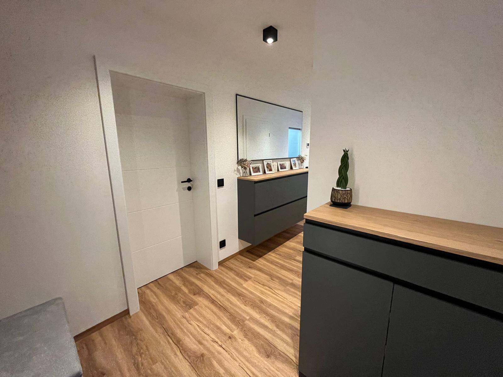 Heller Flur mit Laminatboden, Kommode und Blick auf eine weiße Tür mit modernem Design.