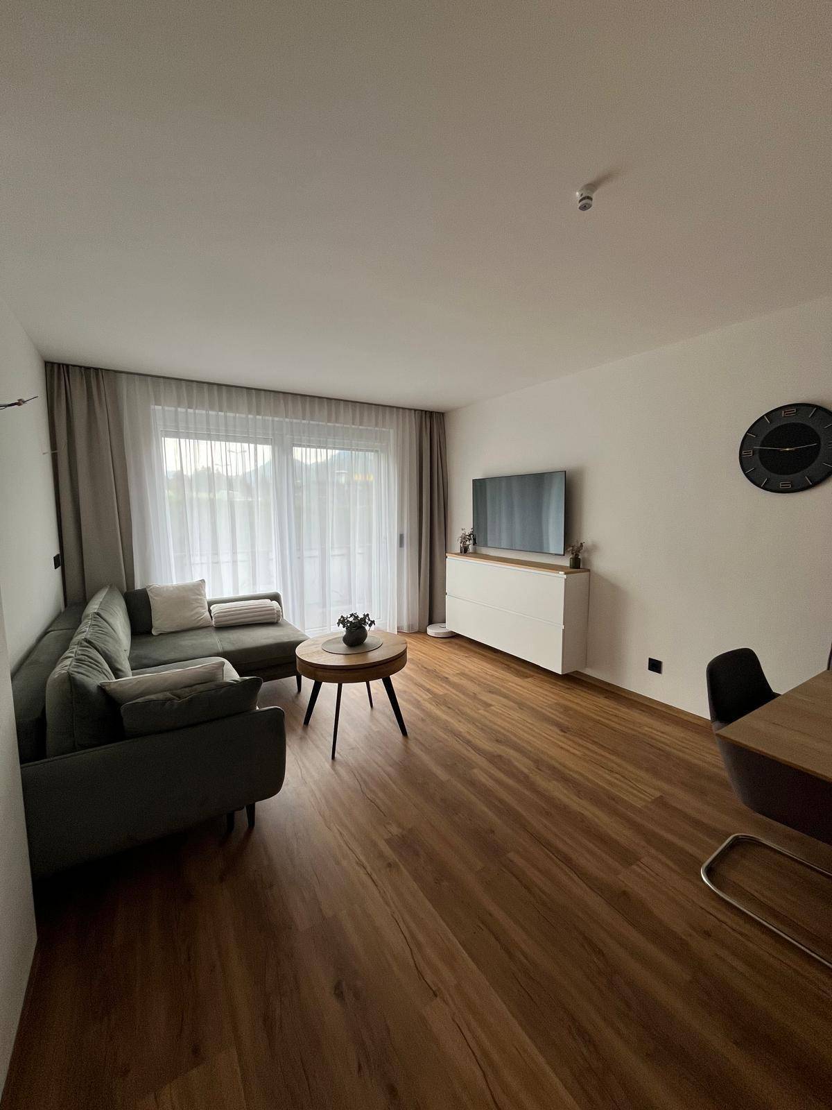 Helles Wohnzimmer mit Sofa, Couchtisch und Blick auf den Balkon durch große Fenster.