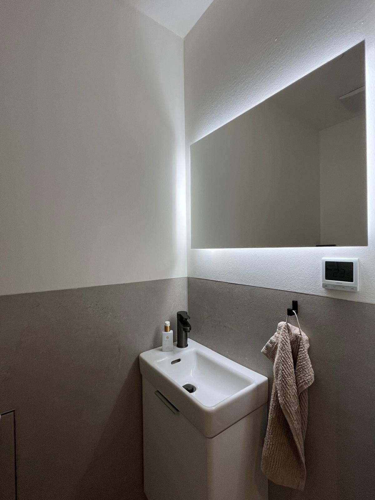 Waschbeckenbereich im Gäste-WC mit beleuchtetem Spiegel über einem modernen Waschtischunterschrank.